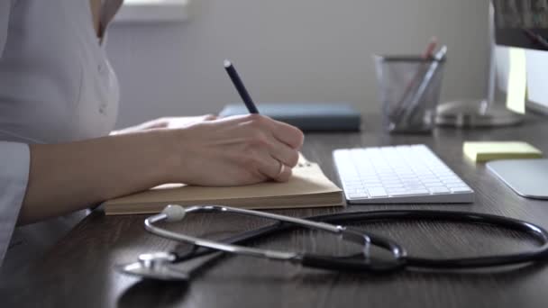 En kvinnlig läkare sitter vid ett bord och skriver ut ett recept till en patient. — Stockvideo