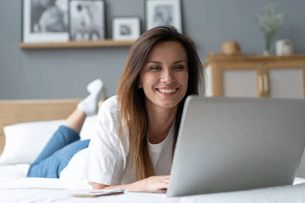 Portrait of a beautiful smiling young woman using laptop in bed at home. — Stock Photo, Image