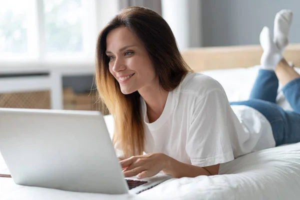 Portrait of a beautiful smiling young woman using laptop in bed at home. — Stock Photo, Image