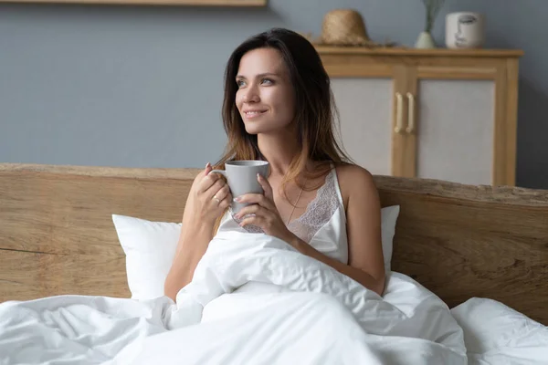 Indah Happy Young Woman minum secangkir kopi atau teh Sementara berbaring di tempat tidur setelah bangun di pagi hari — Stok Foto