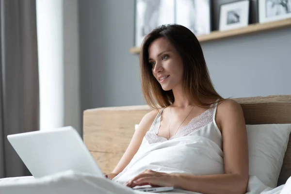Pretty woman using her laptop in bed. — Stock Photo, Image