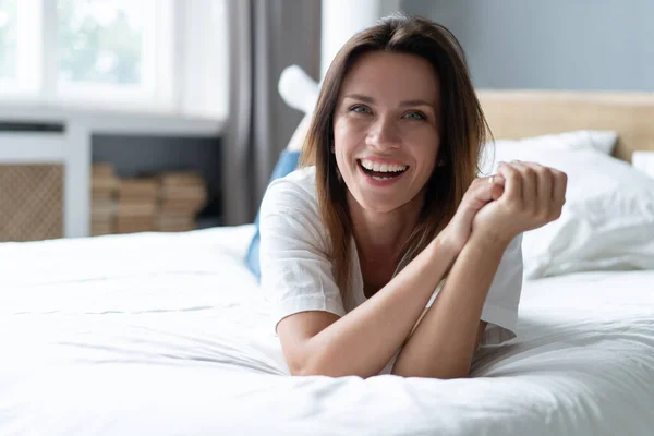 Porträtt av en leende söt ung kvinna liggande i sängen. — Stockfoto