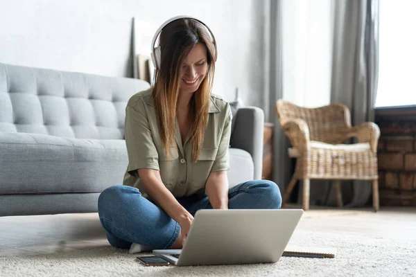 Εμπνευσμένο. Αυτοπεποίθηση νεαρή όμορφη χαμογελαστή γυναίκα που εργάζεται σε φορητό υπολογιστή, ενώ κάθεται στο πάτωμα στο σπίτι. — Φωτογραφία Αρχείου