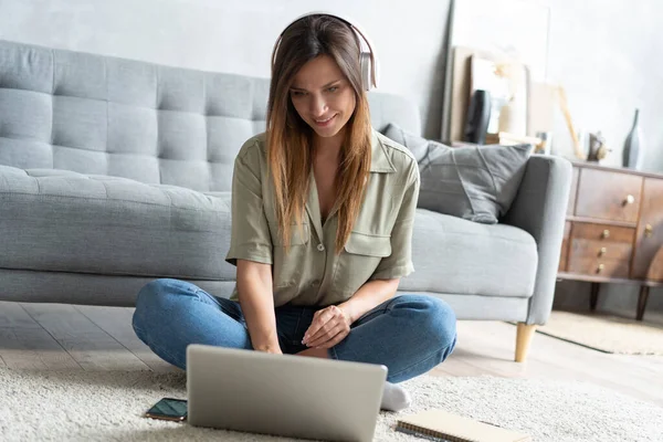 Solo inspirada. Joven confiada hermosa mujer sonriente que trabaja en el ordenador portátil mientras está sentado en el suelo en casa. — Foto de Stock