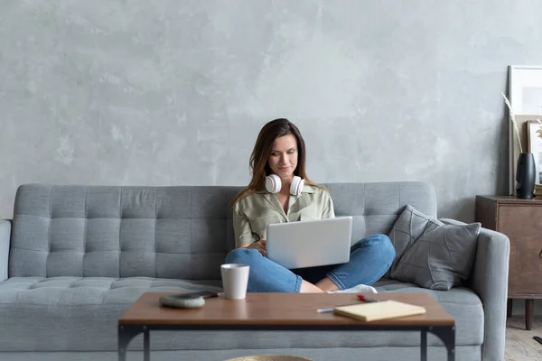 Une jeune femme qui fait des recherches pour son entreprise. Femme souriante assise sur le canapé naviguant sur le site de shopping en ligne — Photo