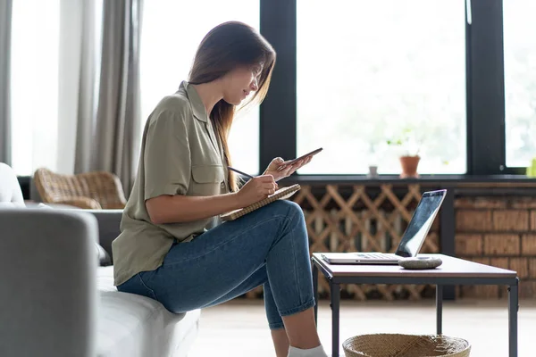 Wanita menggunakan laptop di ruang tamunya. Bekerja dari rumah di karantina kuncian. Jarak sosial. — Stok Foto