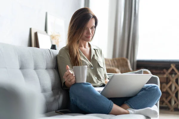 Mujer usando un portátil en su sala de estar. Trabajando desde casa en cuarentena. Distanciamiento social. — Foto de Stock