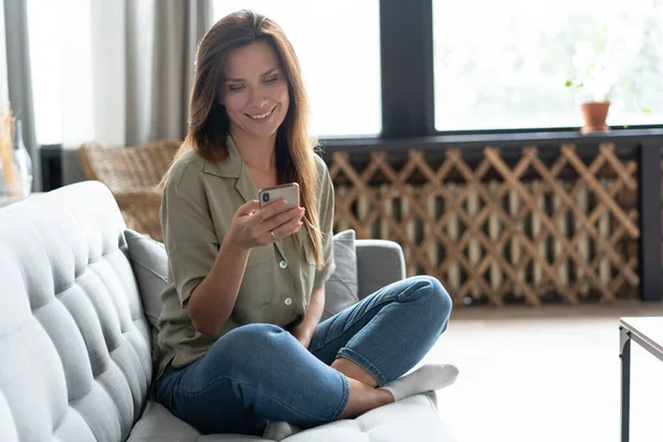 Mujer usando portátil y teléfono móvil en el sofá. — Foto de Stock