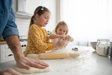 Gülümseyen baba ve kızlar mutfakta yemek pişiriyor ve eğleniyorlar.