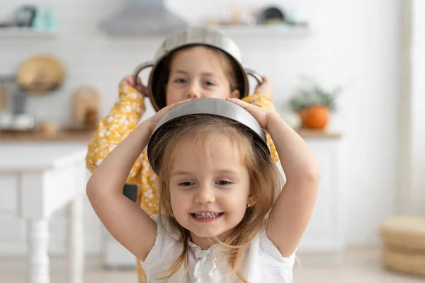 Χαριτωμένα μικρά παιδιά φορώντας μπολ ως κράνος και παίζοντας στο σπίτι. — Φωτογραφία Αρχείου