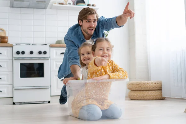 Eccitato felice giovane padre correre spingere scatola di cartone con bambini piccoli simpatici figlie cavalcare dentro, divertendosi. — Foto Stock