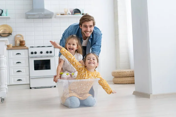 Emocionado feliz padre joven ejecutar empuje caja de cartón con pequeños niños lindos hijas paseo dentro, divertirse. — Foto de Stock