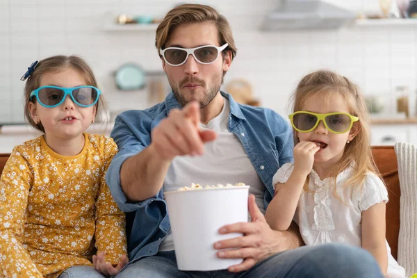 Happy family watching TV at home and eating popcorn.