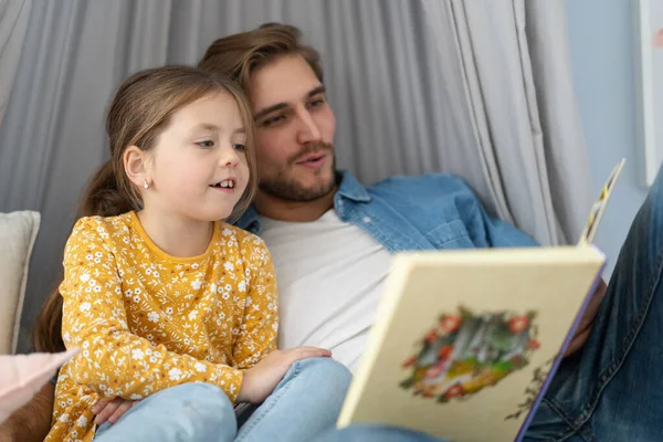침실 바닥에 누워 있는 딸에게 책을 읽어 주는 아버지. — 스톡 사진