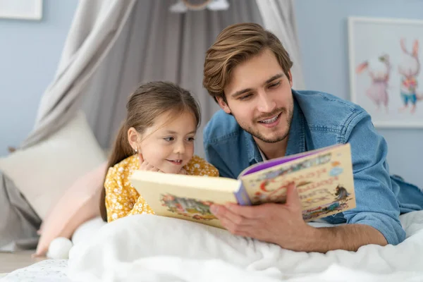 침실 바닥에 누워 있는 딸에게 책을 읽어 주는 아버지. — 스톡 사진
