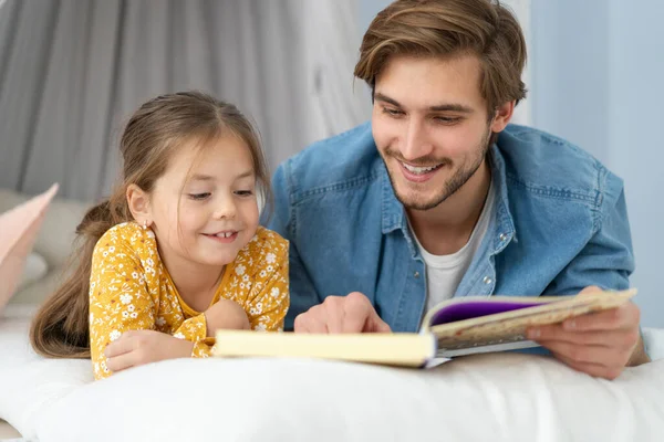 Father reading a book to his daughter while lying on the floor in bedroom. — Stock Photo, Image