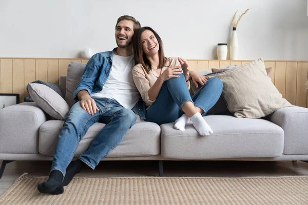 Feliz joven pareja caucásica relajarse en el sofá acogedor en casa abrazos mirada en la distancia soñando juntos — Foto de Stock