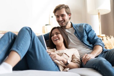 Evdeki kanepede oturan genç çift, internet ve sosyal medya için tablet bilgisayar kullanıyorlar..