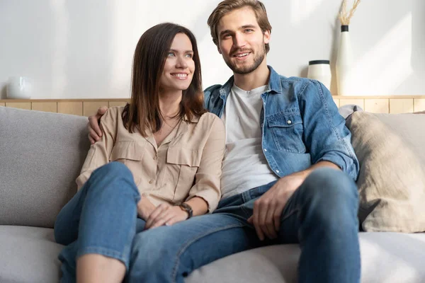 Feliz joven pareja caucásica relajarse en el sofá acogedor en casa abrazos mirada en la distancia soñando juntos — Foto de Stock
