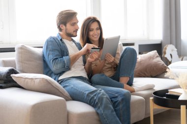 Oturma odasındaki tabletle kanepede oturmuş internetten alışveriş yapan gülen çift..