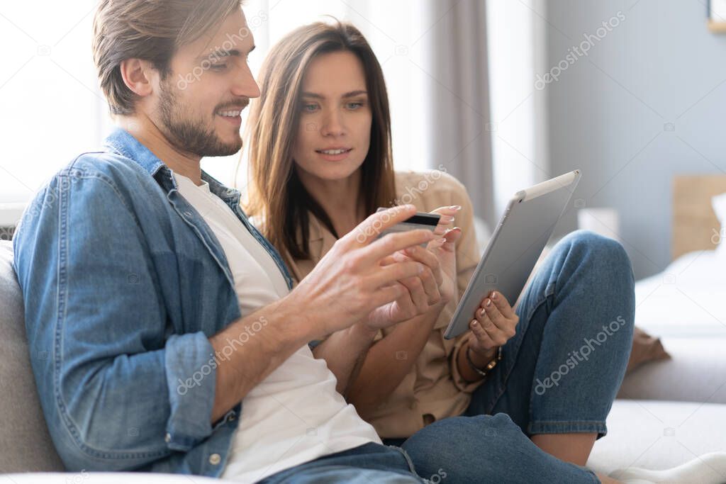 Laughing couple sitting on the couch shopping online with tablet pc at home in the living room.