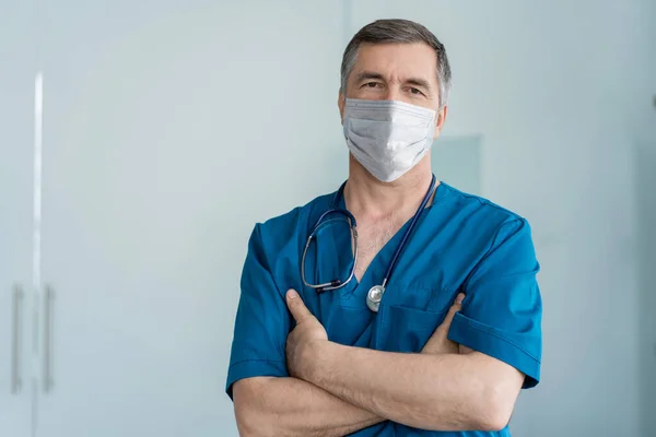 Χαρούμενος ώριμος γιατρός με μάσκα προσώπου στέκεται στο νοσοκομείο, την υγειονομική περίθαλψη και την ιατρική. — Φωτογραφία Αρχείου