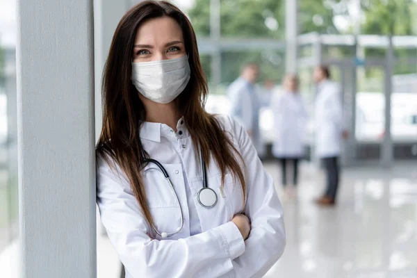 Portret van een jonge vrouwelijke arts met medisch masker die in het consult naar de camera kijkt — Stockfoto