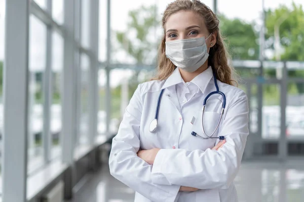 Portret van een jonge vrouwelijke arts met medisch masker die in het consult naar de camera kijkt — Stockfoto