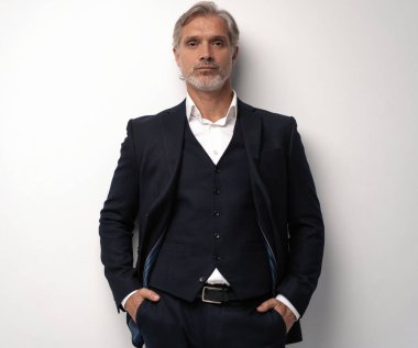 Gri arkaplana karşı poz veren orta yaşlı yakışıklı bir adam.