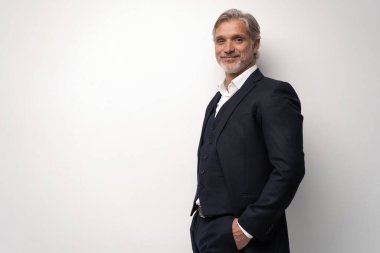 Gri arkaplana karşı poz veren orta yaşlı yakışıklı bir adam.