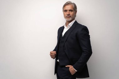 Gri arkaplana karşı poz veren orta yaşlı yakışıklı bir adam.