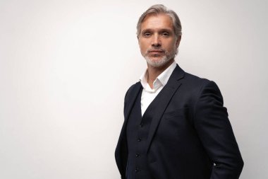 Gri arkaplana karşı poz veren orta yaşlı yakışıklı bir adam.