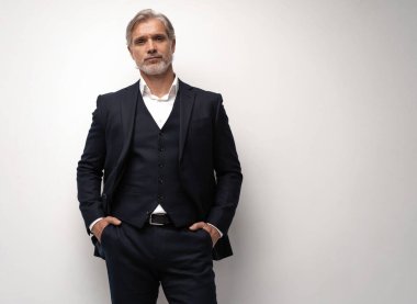 Gri arkaplana karşı poz veren orta yaşlı yakışıklı bir adam.