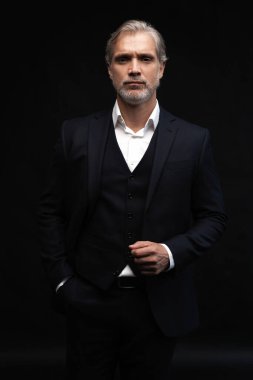 Siyah arkaplanda poz veren orta yaşlı yakışıklı bir adam.