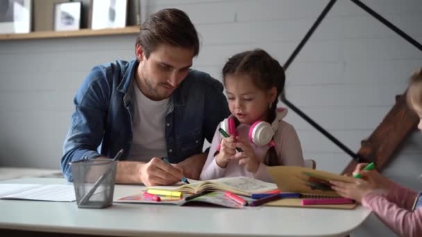 Ayah muda membantu putri kecil dengan pekerjaan rumah, duduk bersama di meja — Stok Video