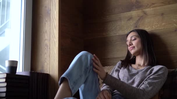 Avslappnad ung kvinna dricka kaffe eller te från en mugg medan du sitter på soffan — Stockvideo