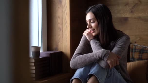 Расслабленная молодая женщина пьет кофе или чай из кружки, сидя на диване — стоковое видео