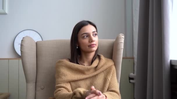 Mulher mestiça indiana atraente olhando para a câmera sentar-se no sofá sozinho em casa — Vídeo de Stock