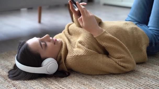 Mujer india de raza mixta en auriculares escuchando música favorita sosteniendo el teléfono — Vídeos de Stock