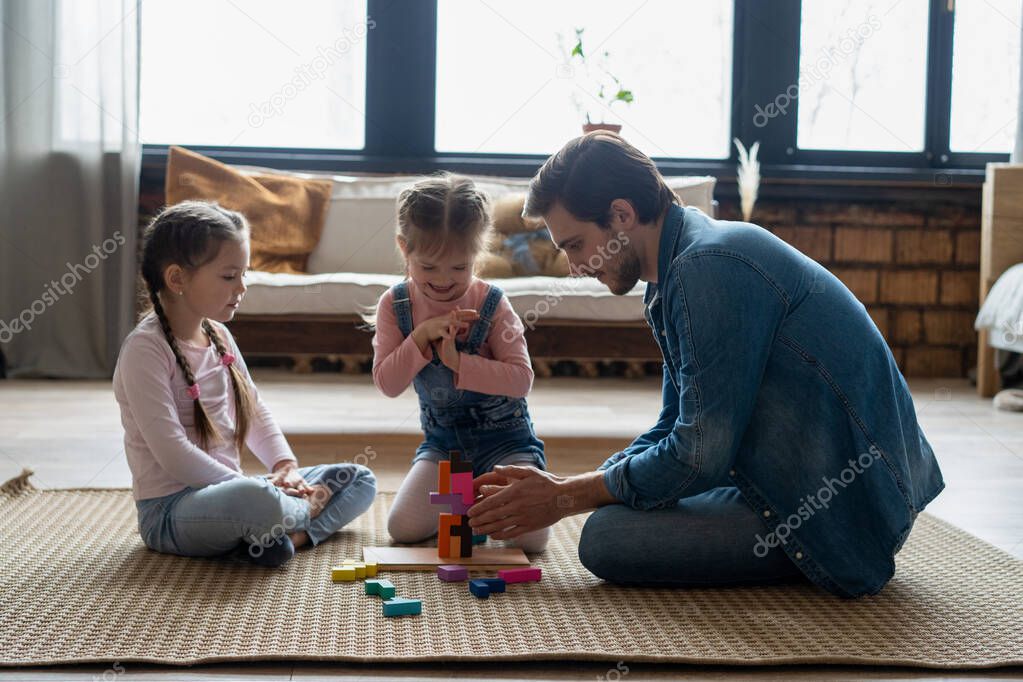 Loving young father lying on floor with small kids have fun engaged in funny activity with construction bricks