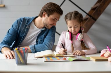 Küçük kızına okul için ödevlerini yapmasına yardım eden bir baba.