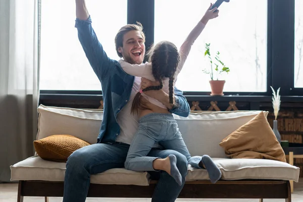 family, gaming and entertainment concept - happy father and little daughter with gamepads playing video game at home.