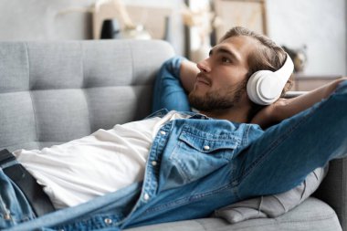 Orta yaşlı bir adam kulaklıkla müzik dinliyor. Evindeki kanepede dinleniyor..