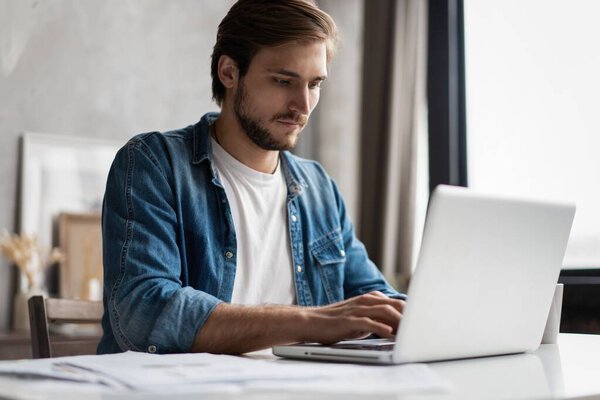 Successful entrepreneur smiling in satisfaction as he checks information on his laptop computer while working
