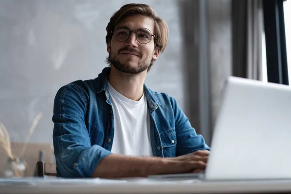 Successful entrepreneur smiling in satisfaction as he checks information on his laptop computer while working