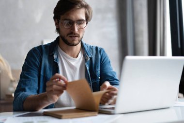 Ciddi bir iş adamı, gözlüklü, bilgisayarını evde kullanıyor ve not alıyor..