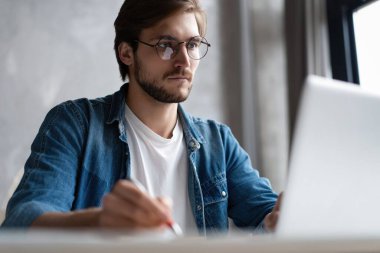 Ciddi bir iş adamı, gözlüklü, bilgisayarını evde kullanıyor ve not alıyor..