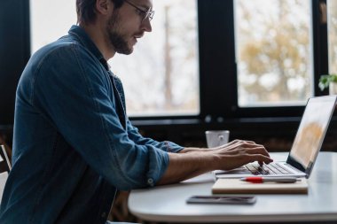 Genç serbest çalışan, dizüstü bilgisayar kullanan, evde çalışan mutlu, not defterinde yazan biri.