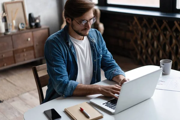 Young man freelancer using laptop studying online working from home, happy casual guy typing on notebook