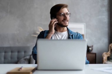 Pazarlama müdürü danışman müvekkil teklif sunuyor ev ofisinin laptopunun yanında telefonla konuşuyor.